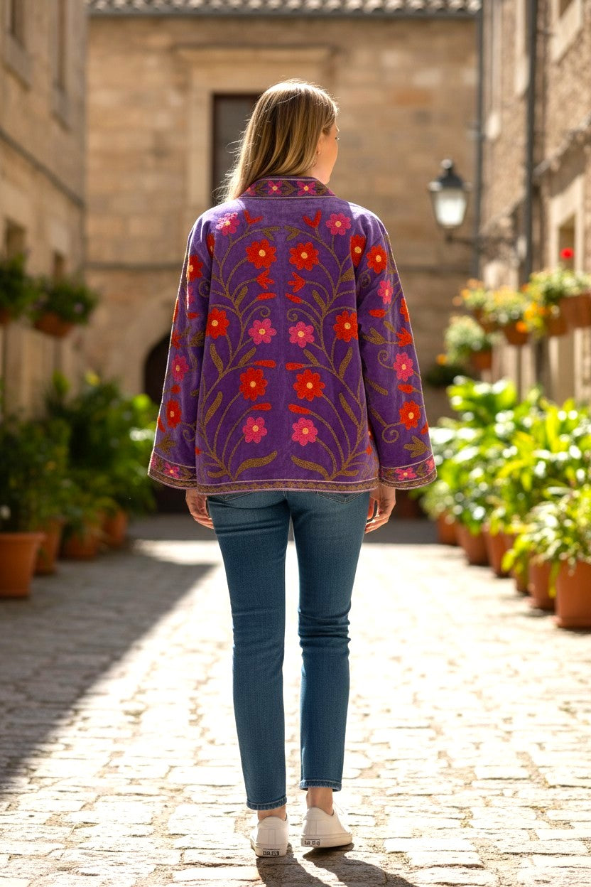 Model wearing a Les Sûtras Velvet Suzani - Embroidered Jacket - Mauve walking down a sunlit street.